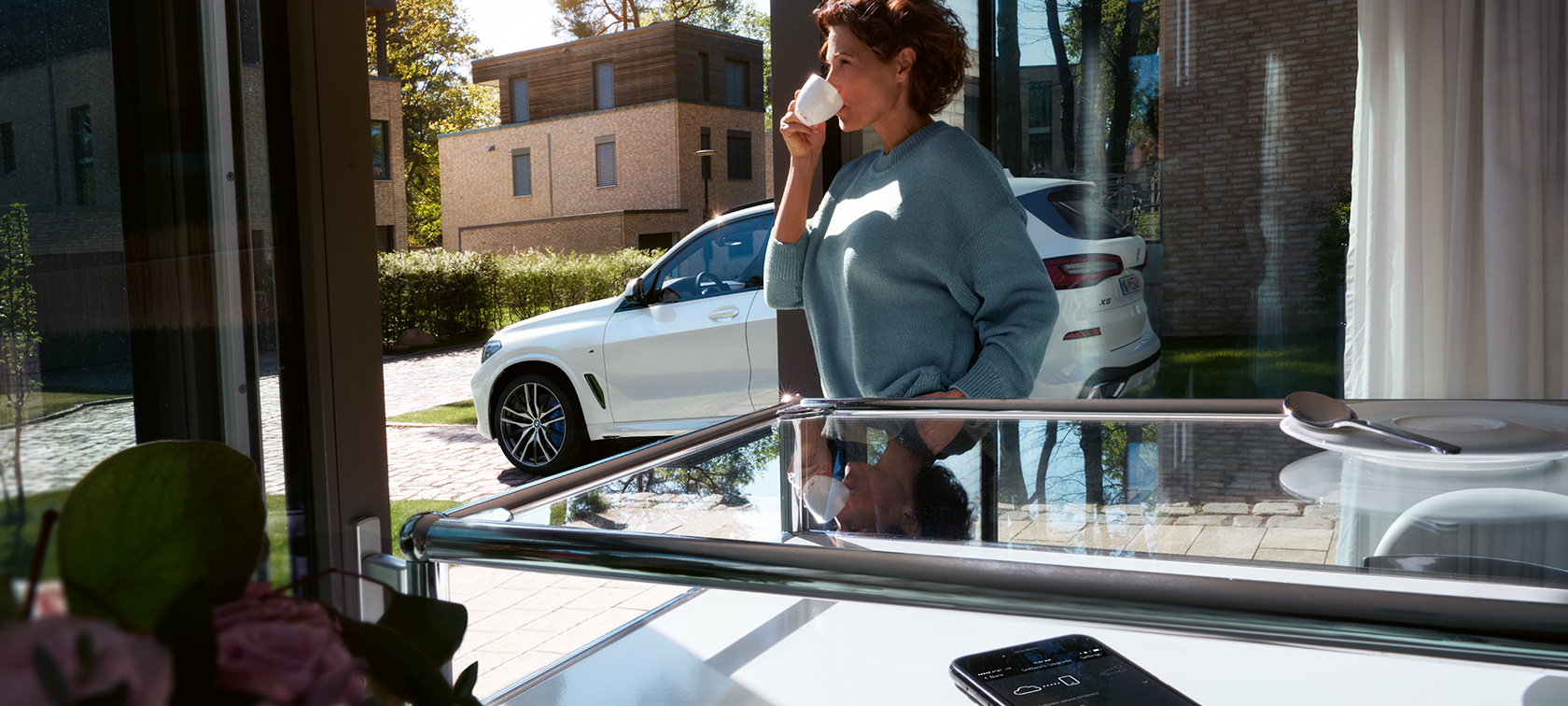 BMW Remote Software Upgrade Una mujer bebe de una taza mientras BMW Remote Software Upgrade actualiza el software de su BMW X5