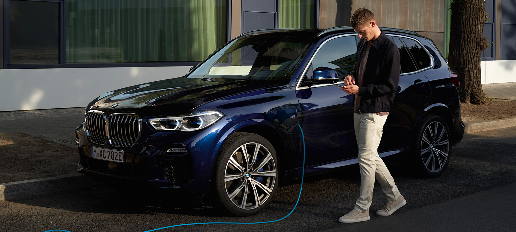 Una mujer utiliza My BMW App en su smartphone Un hombre utiliza My BMW App de BMW ConnectedDrive en el smartphone mientras se carga su BMW X5 Híbrido Enchufable