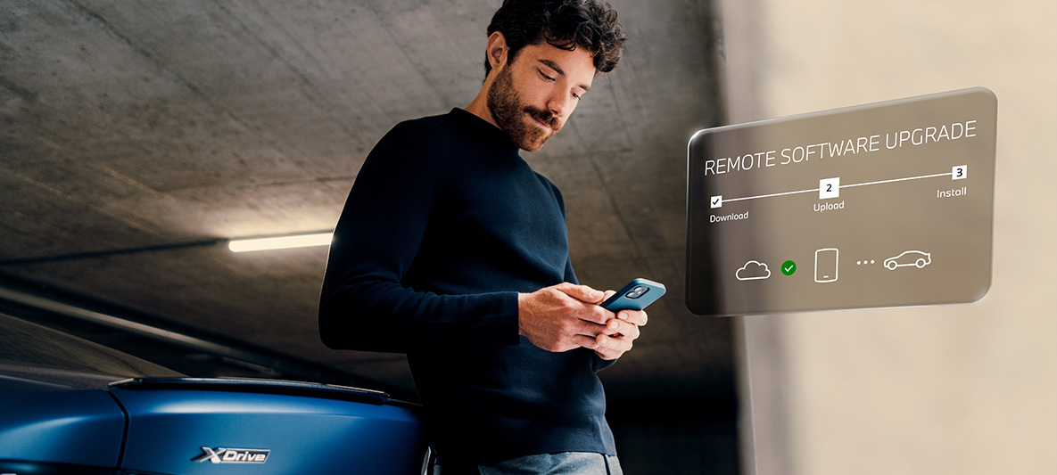 Hombre apoyado en la zaga de un BMW mirando su smartphone Remote Software Upgrade, hombre apoyado en la zaga de un BMW mirando su smartphone