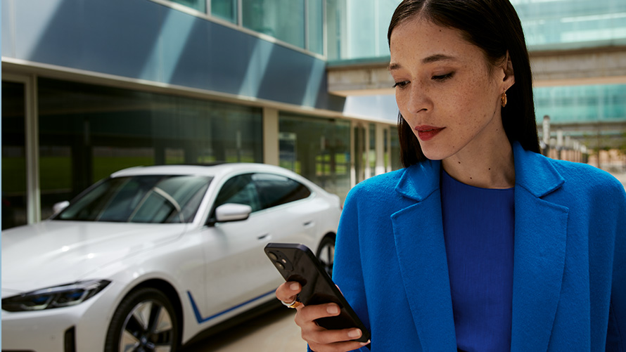 Mujer de pie delante de un BMW Mujer de pie delante de un BMW mirando su smartphone