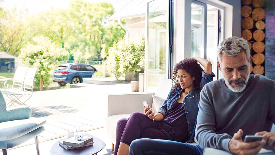 Servicios Remotos Un hombre y una mujer sentados en el sofá utilizan los Servicios Remotos en sus smartphones