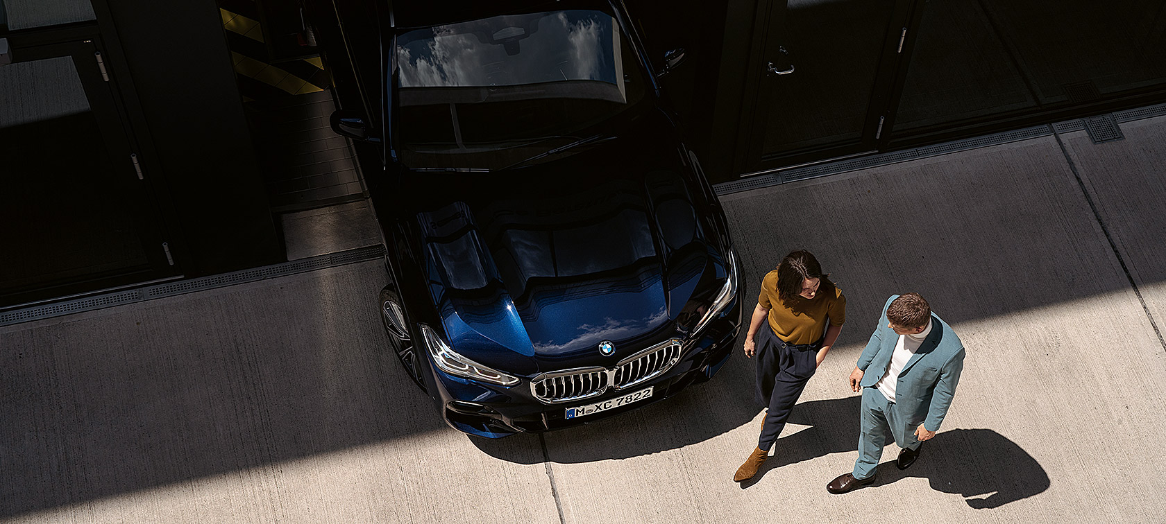 Una mujer y un hombre pasan por delante del BMW Vista aérea de una mujer y un hombre pasando por delante de un BMW