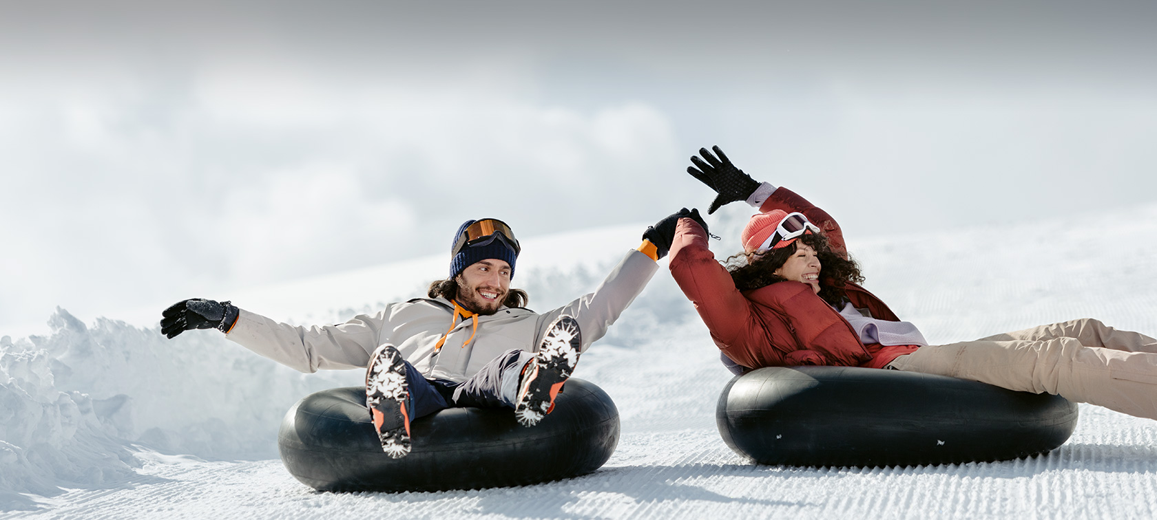 Accesorios Originales BMW y BMW Service para otoño e invierno Mujer y hombre riendo sobre neumáticos a modo de trineo en la nieve