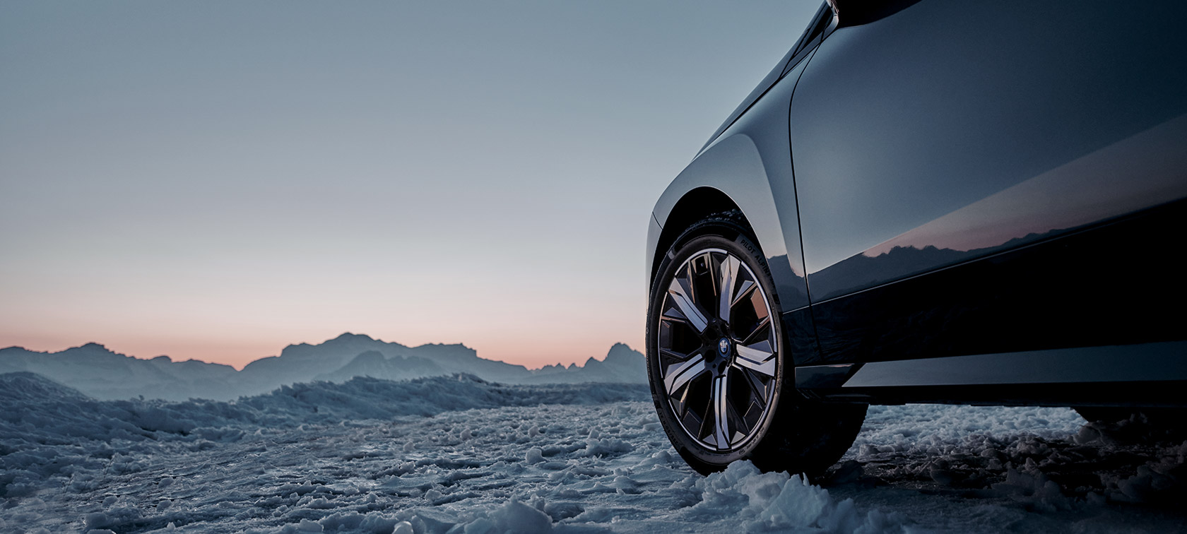 Llantas originales BMW en el BMW iX (I20) sobre nieve delante de montañas Llantas originales BMW en el BMW iX (I20) sobre nieve delante de montañas
