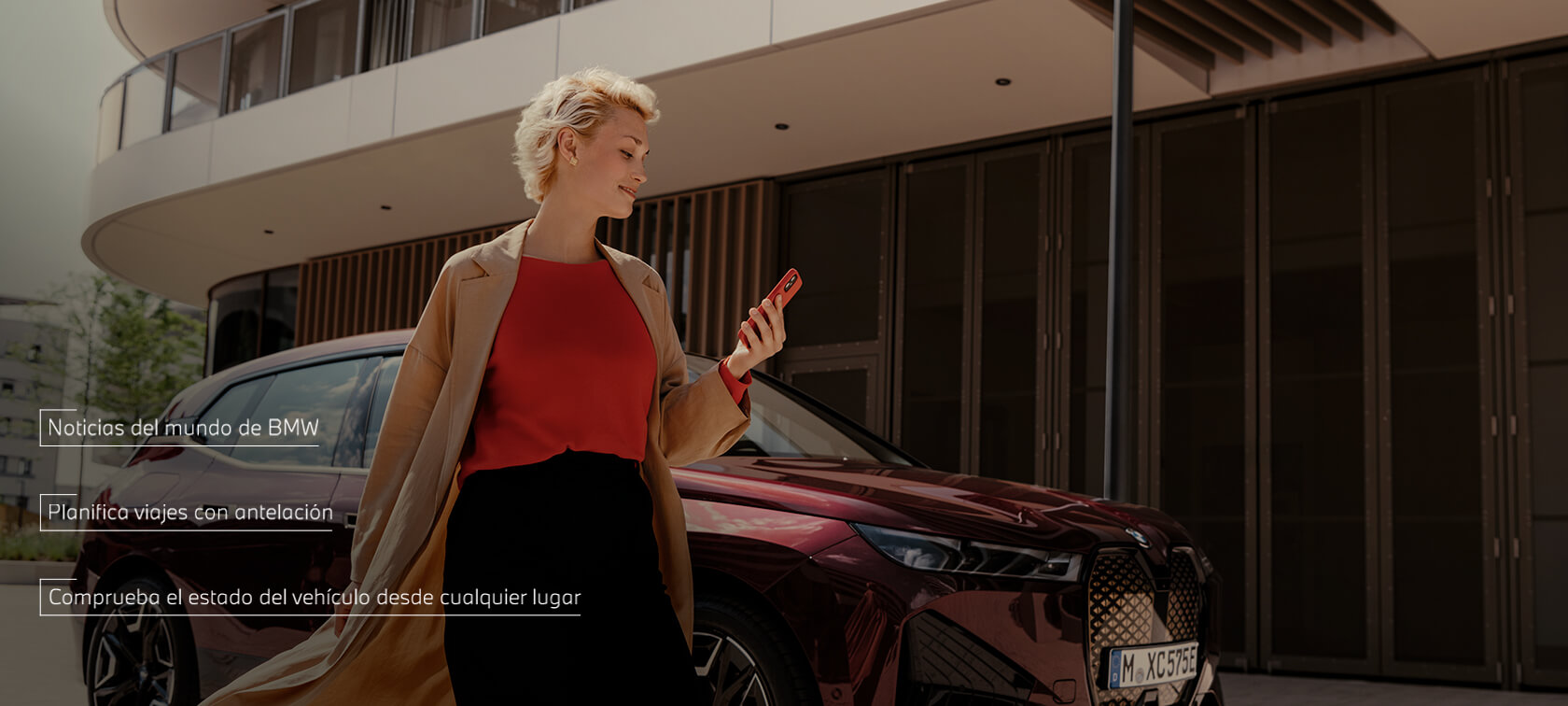 Una mujer de pie delante de un BMW X5 blanco utiliza My BMW App en el smartphone