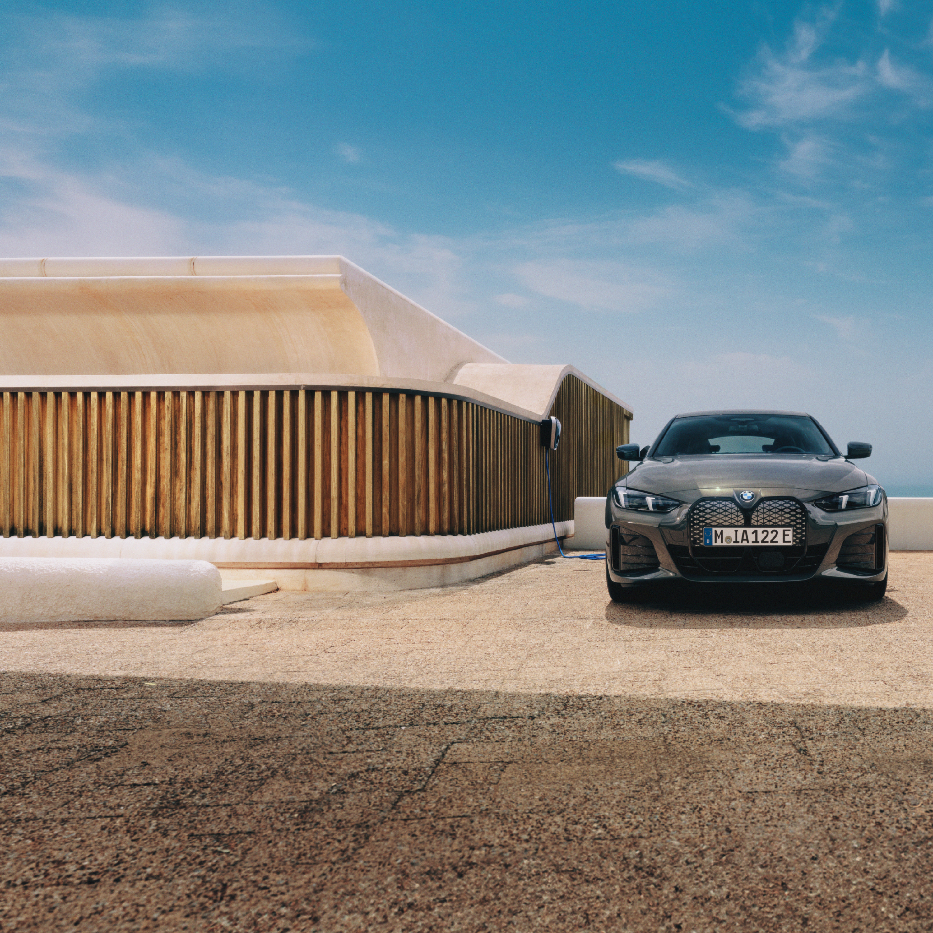 Un hombre con un smartphone de pie junto a un BMW i4 conectado a un Wallbox