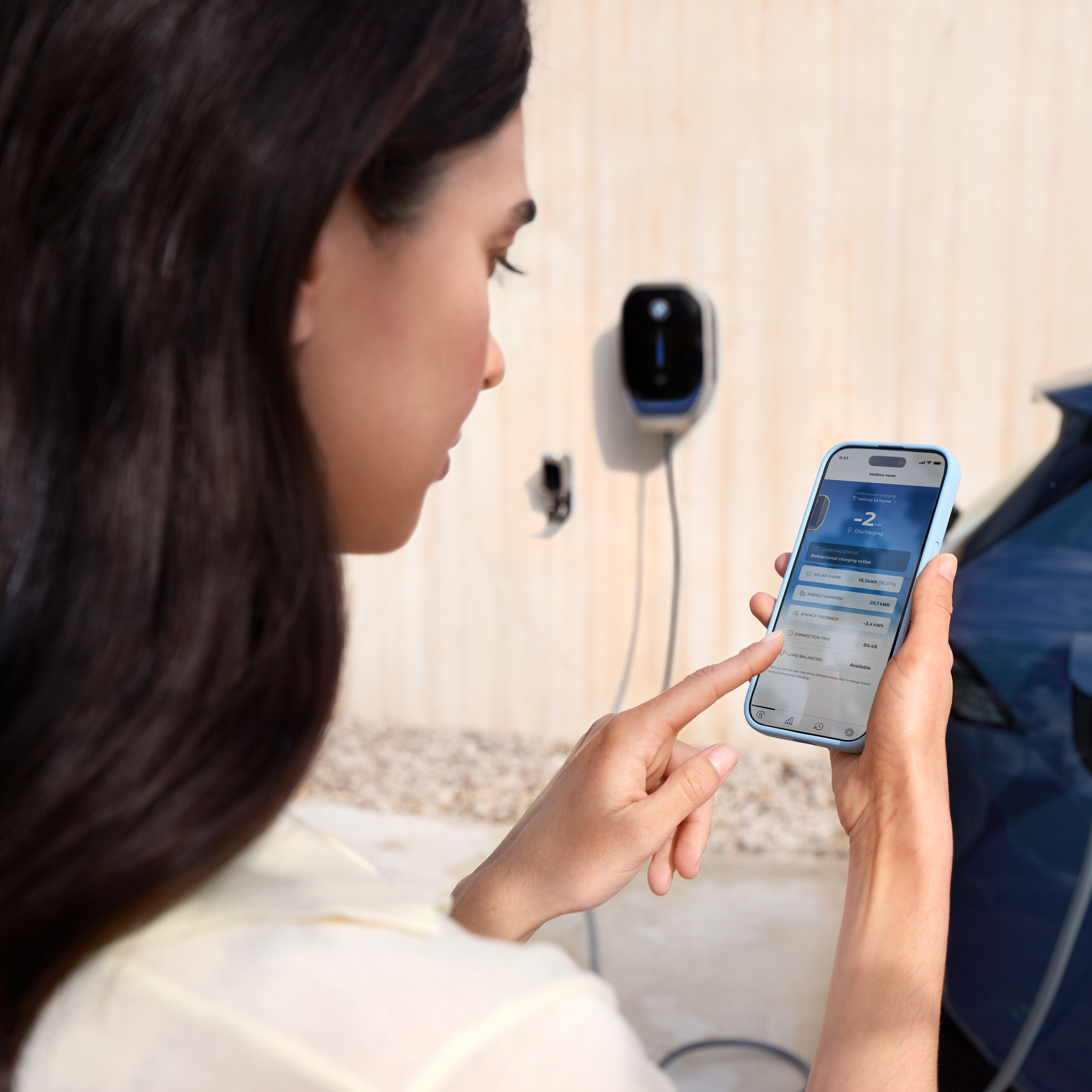 Una mujer mirando su smartphone y un BWM Wallbox en segundo plano